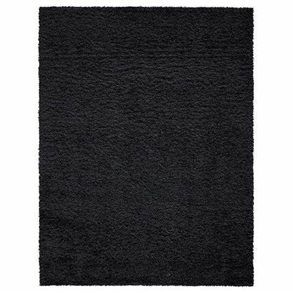 black rug with a textured, shaggy surface, evoking a sense of warmth and comfort. Its minimalistic style suggests modern decor.