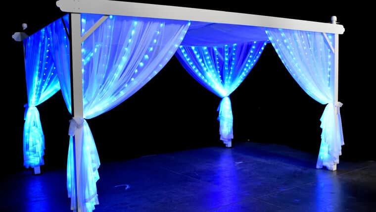 LED Cabana Blue draped with translucent curtains, backlit by vibrant blue LED lights against a dark background, creating a serene and magical ambiance.