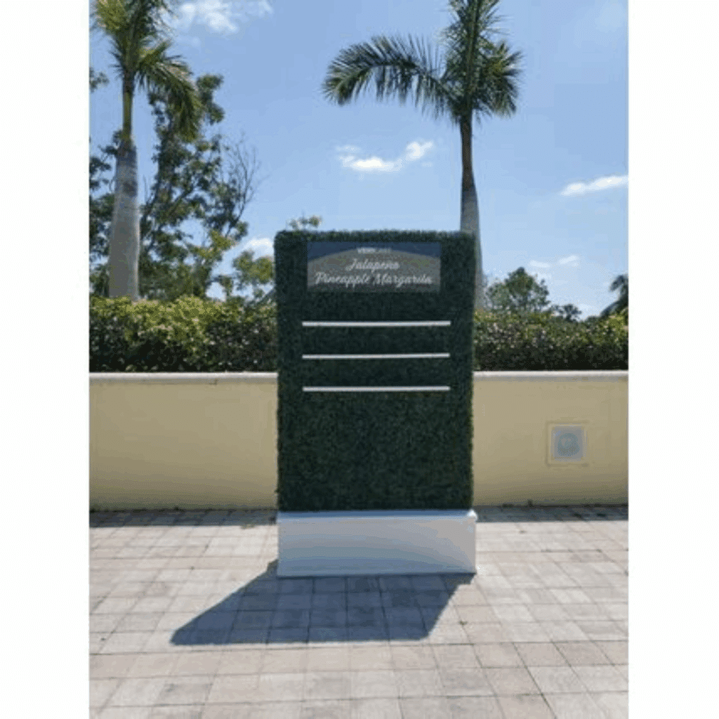 Hedge Wall Shelves with green foliage background and white text, "Jalapeno Pineapple Margarita," set against a sunny backdrop of palm trees and a clear sky.